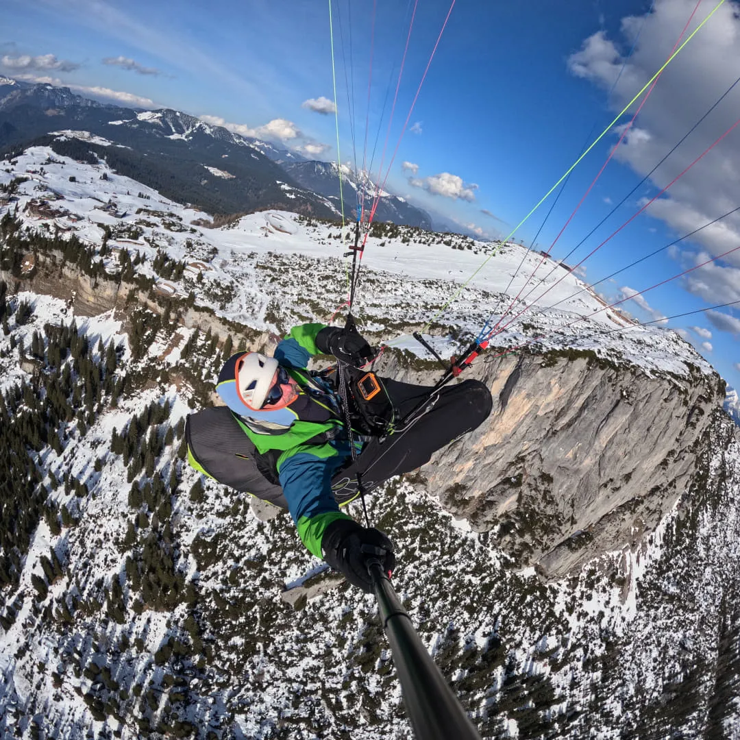 Person beim Paragliding über verschneiten Bergen