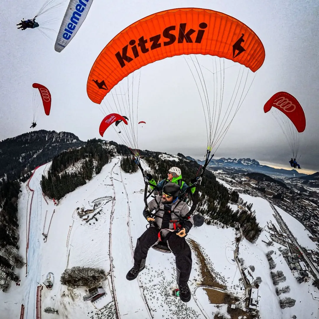 Paraglider über schneebedecktem Gelände, KitzSki-Schild sichtbar