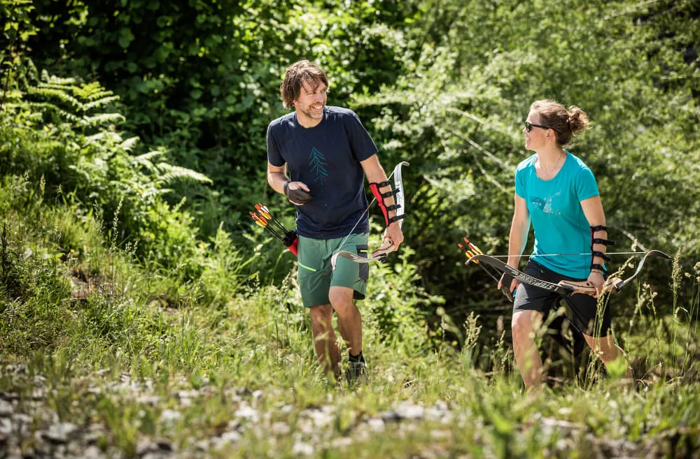Zwei Personen wandern im Freien mit Bögen und Pfeilen.